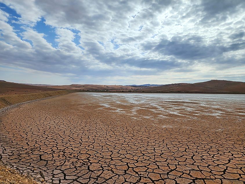 The barren expanse of the dry lake under a brooding, overcast sky evokes a sense of desolation and mystery, with its cracked, parched surface reflecting the harshness of an arid environment.