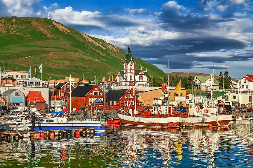 Beautiful view of the historic town of Husavik with traditional colorful houses and traditional fisherman boats lying in the harbor in golden evening light at sunset, northern coast of Iceland